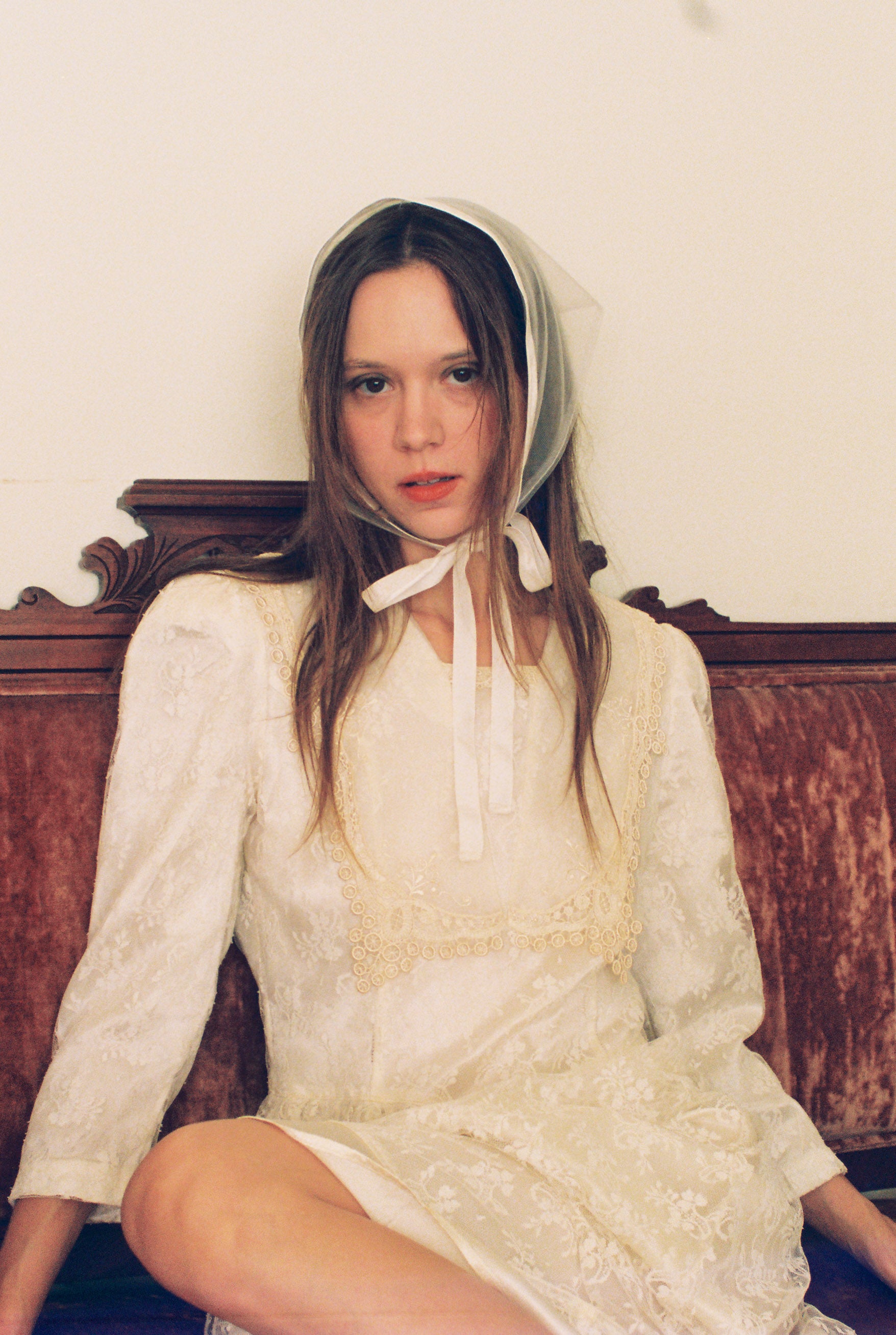 Woman wearing a white lace dress and bonnet sitting on a wooden bench.