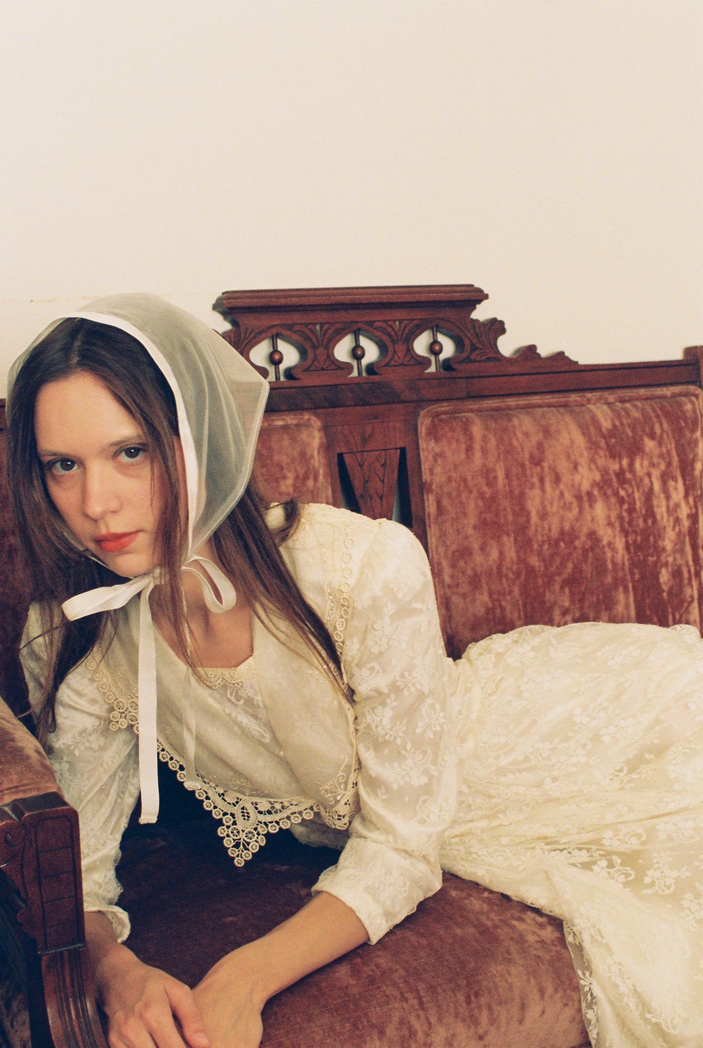Woman wearing a white lace bonnet and dress sitting on an old wooden bed.