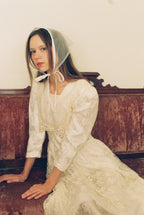 Woman in a white lace dress and bonnet sitting on a wooden bench.
