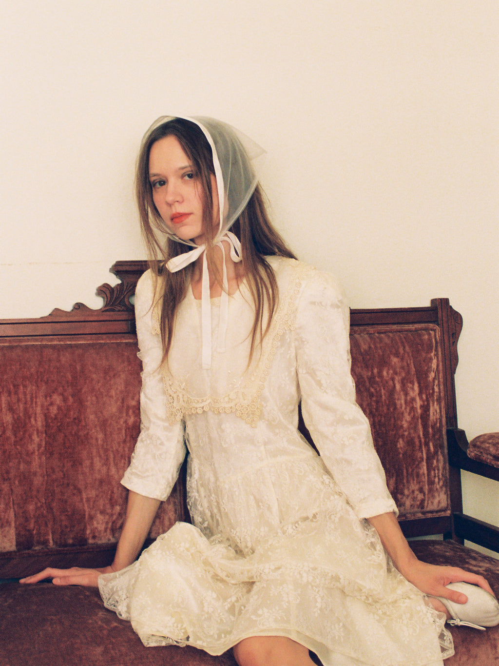Woman in a white dress and bonnet sitting on a wooden bench.