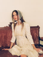 Woman in a white dress and bonnet sitting on a wooden bench.