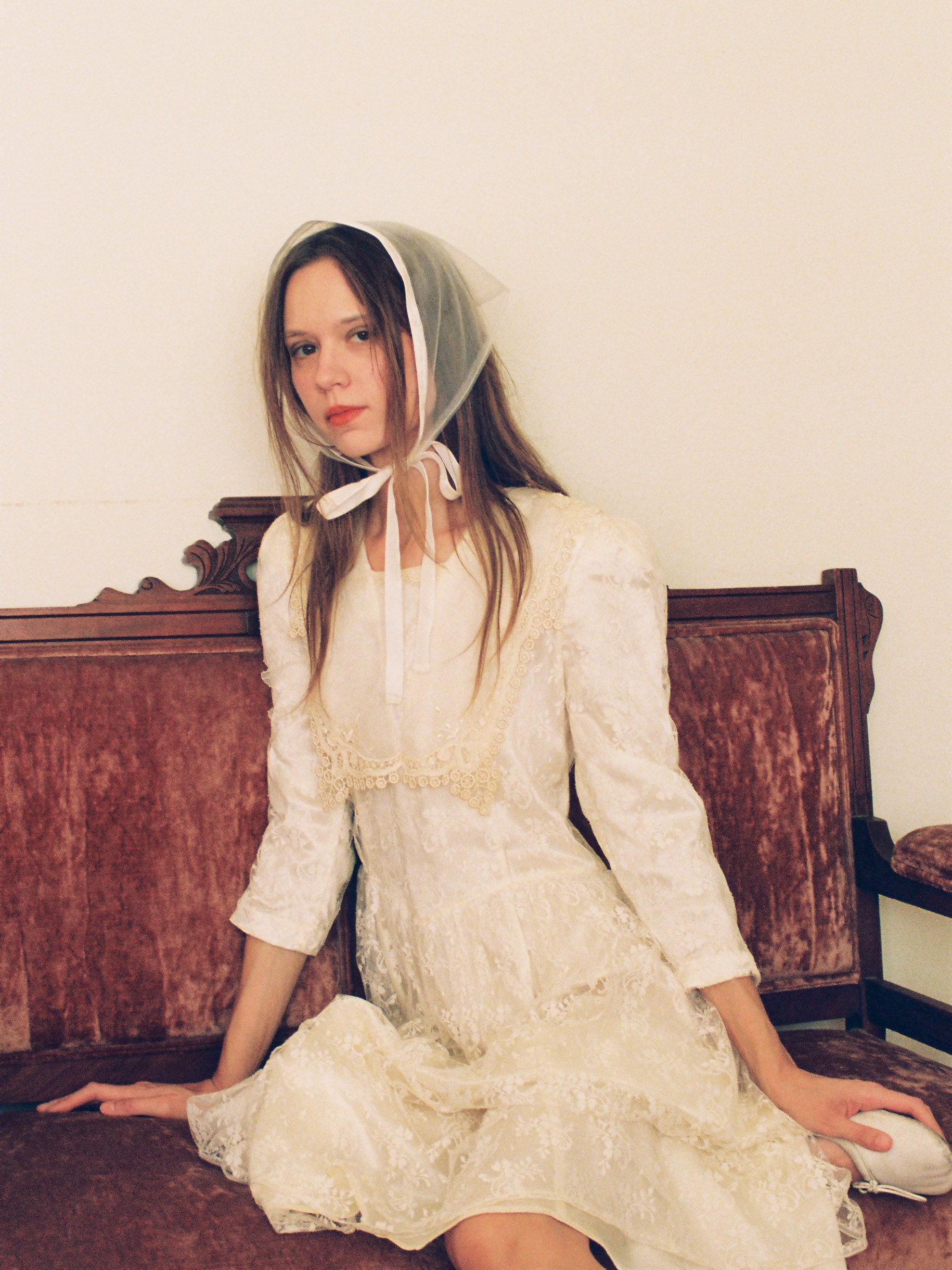Woman in a white dress and bonnet sitting on a wooden bench.