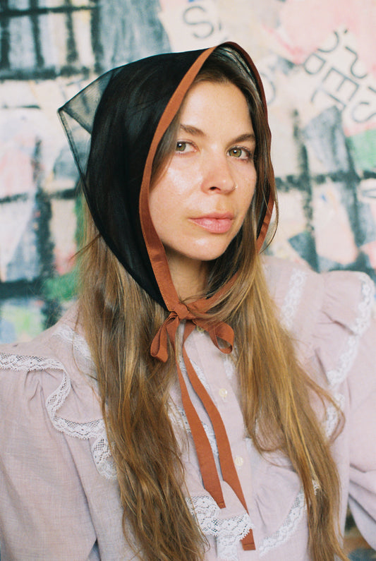 Woman wearing a black bonnet with a brown ribbon against a colorful abstract background