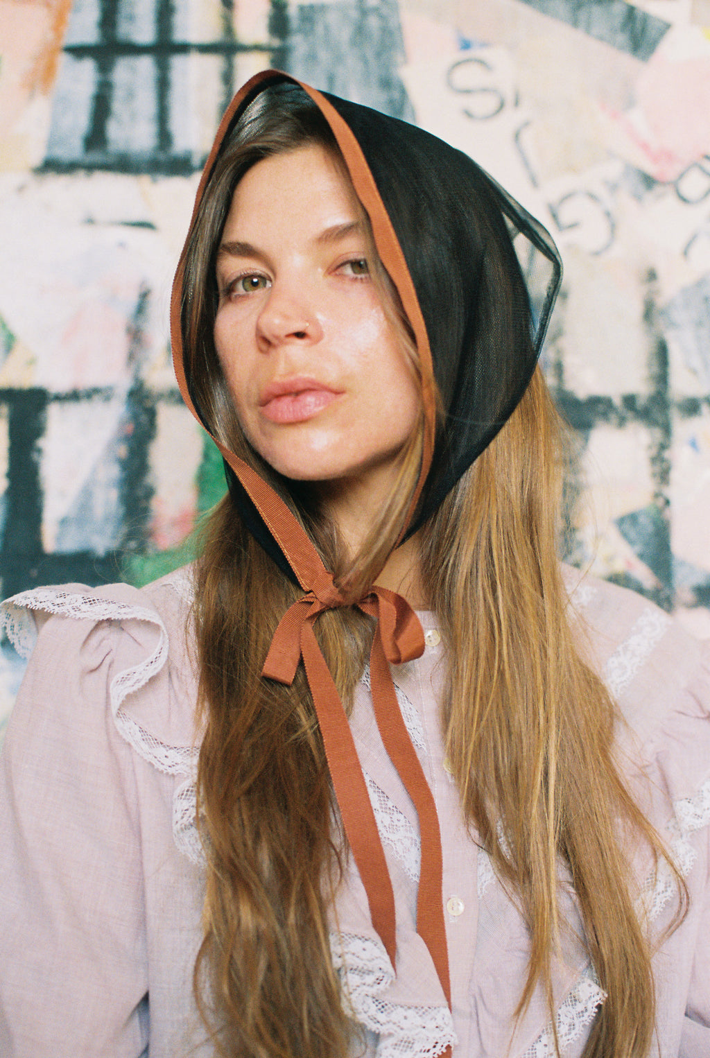 Woman wearing a black bonnet with a brown ribbon against a colorful abstract background