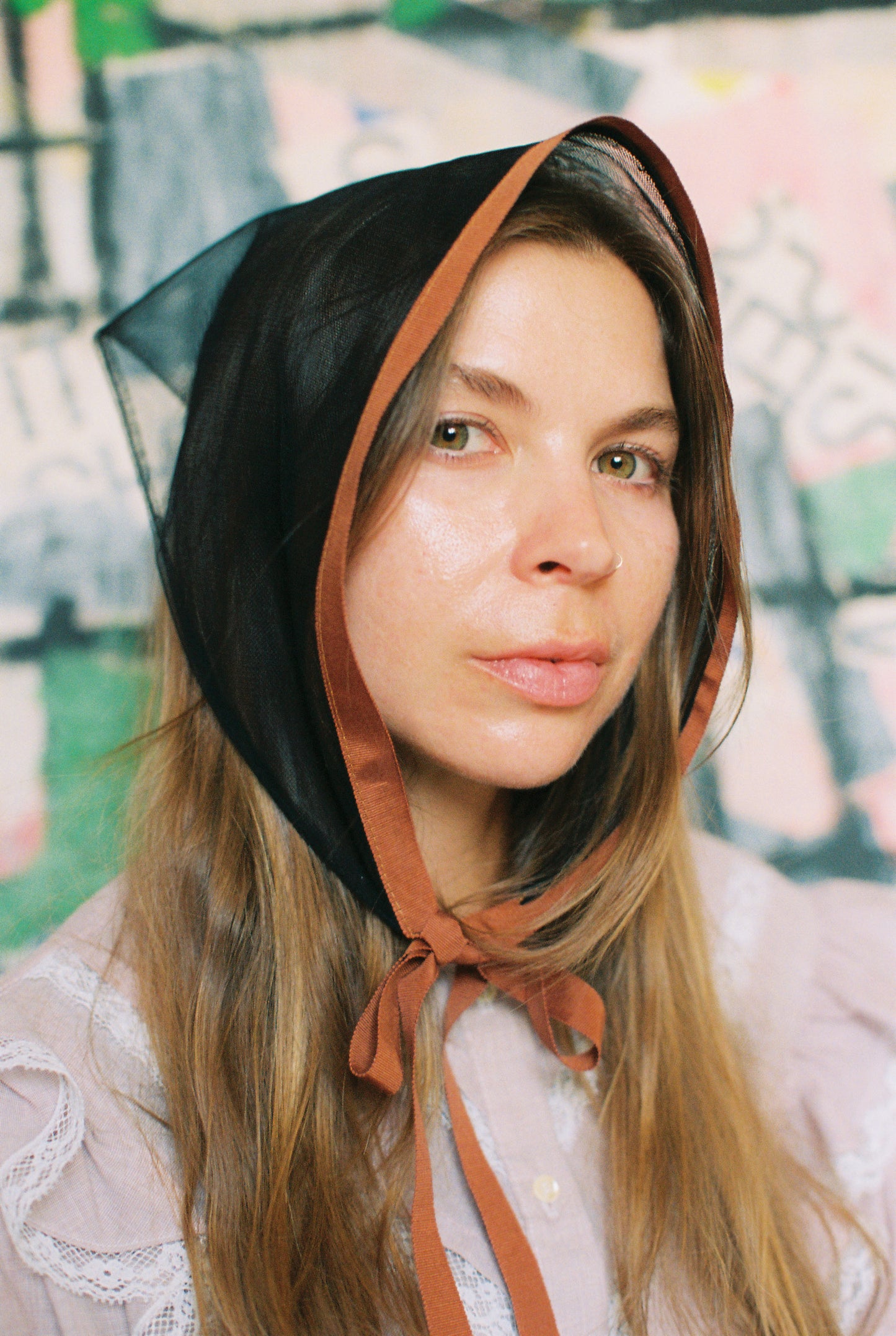 Woman wearing a black headscarf with a brown ribbon against a colorful abstract background