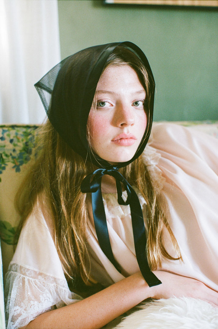 Young girl wearing a black bonnet sitting on a couch with a green wall in the background