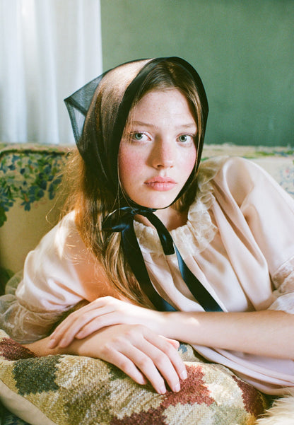Young girl wearing a bonnet sitting on a patterned couch.
