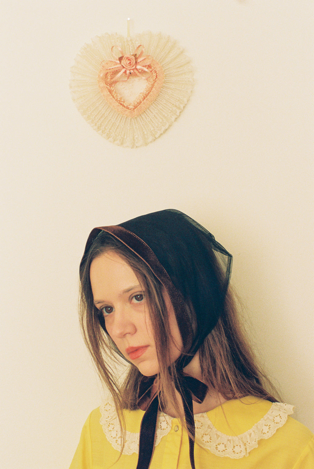 Person wearing a black headscarf with a yellow garment against a plain background