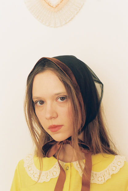 Woman wearing a black headscarf and yellow blouse with lace details on a white background