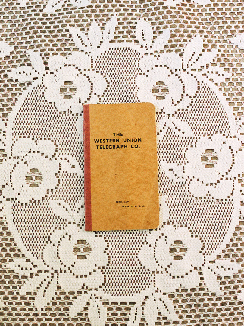 Small tan book titled 'The Western Union Telegraph Co' on a lace tablecloth